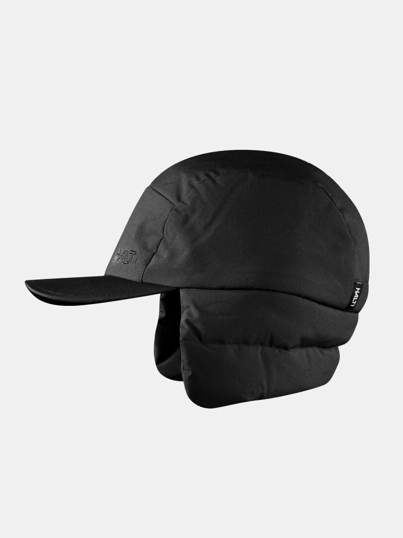 Halti Huove Puffy Hatt, svart vintermössa med fleecefoder, platt skärm och vadderade öronlappar på grå bakgrund.