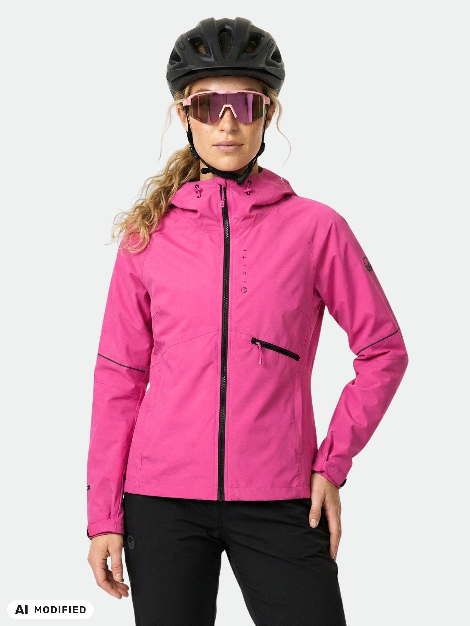 En person klädd i en Halti Shelter Stormwall 3L-jacka för damer, svart hjälm och rosa solglasögon står framför en enfärgad bakgrund.