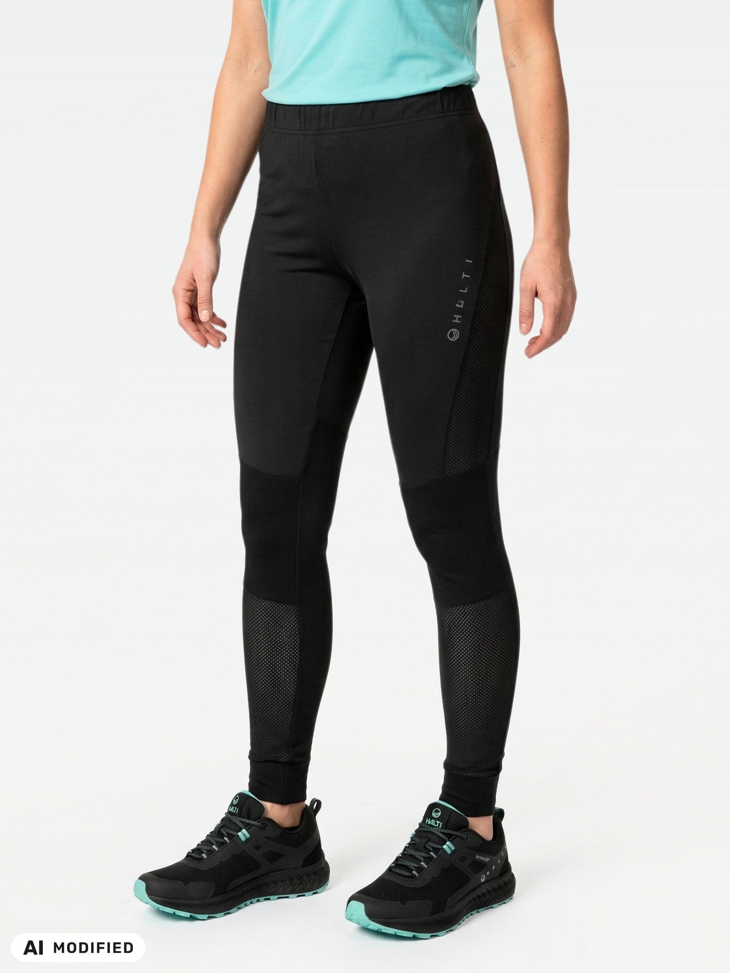 En person i ljusblå skjorta, Halti Tracks Seamless Tights Dam och svarta skor står framför en enfärgad bakgrund.