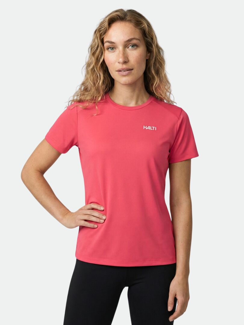 En kvinna i rosa Halti Salves T-skjorta Dam och svarta byxor står med ena handen på höften.