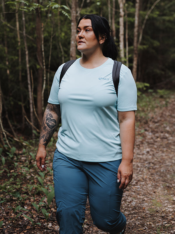 En person i en Halti Salves T-skjorta Dam Plus tillverkad av återvunnen polyester vandrar på en skogsstig med en ryggsäck.