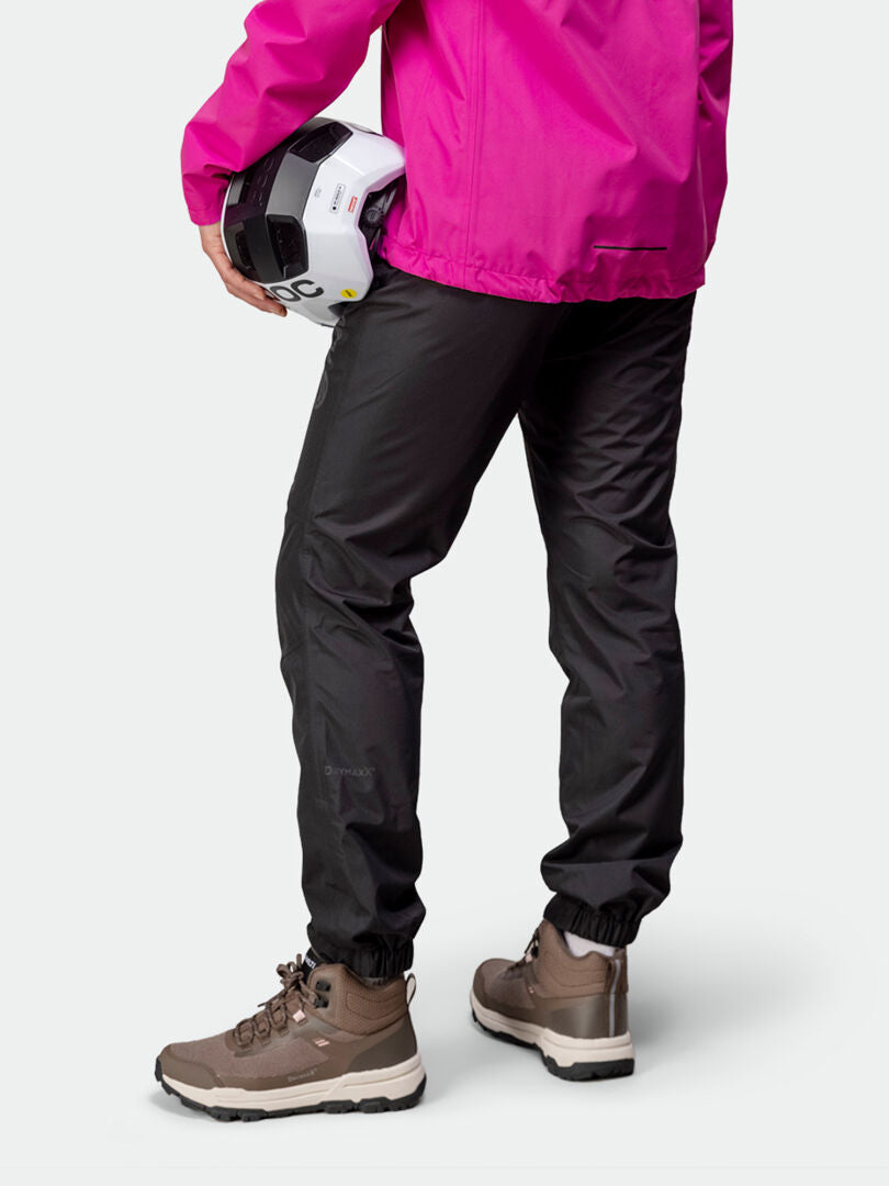 Kvinna i Halti Triant DX Cykelbyxor Dam, beige vandringskängor och en knallrosa jacka i återvunnen polyester, sedd bakifrån.