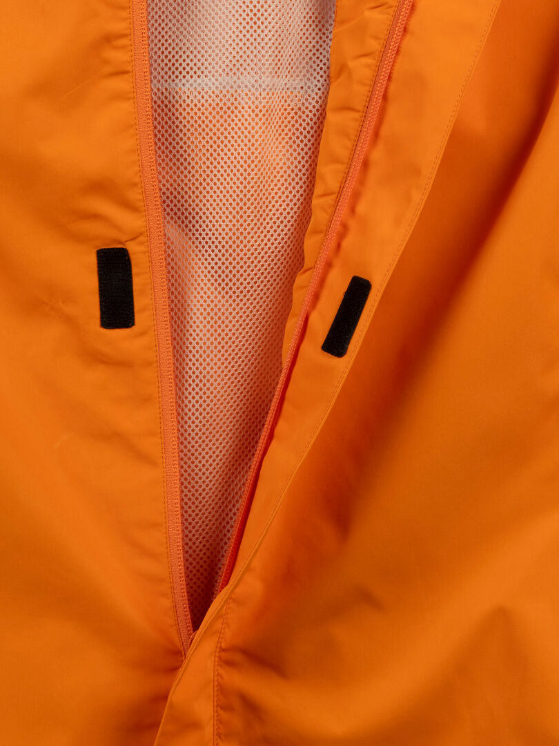 Närbild av Halti Triant DX Cykeljacka Herr: orange med nätfoder, reflexdetaljer och svarta tygflikar vid dragkedjan.