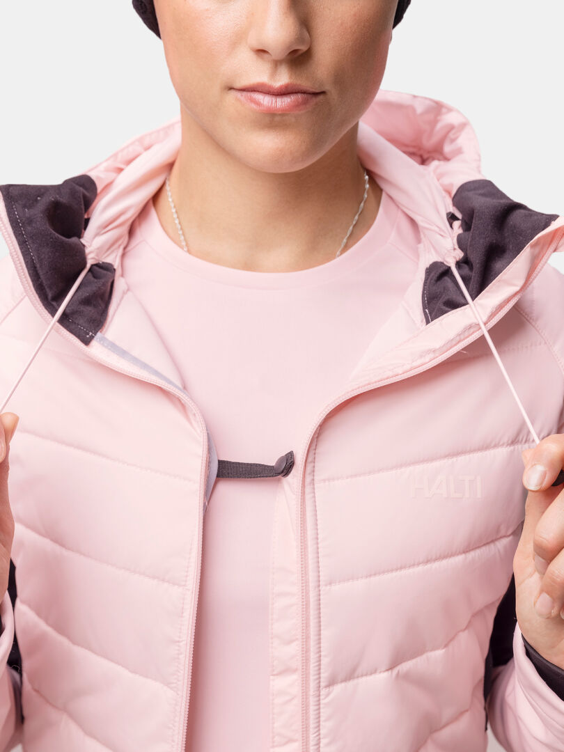 En person i vintersportkläder bär en rosa Halti Hanki 2 Hybrid Längdskidjacka Dam och håller i gula skidstavar.