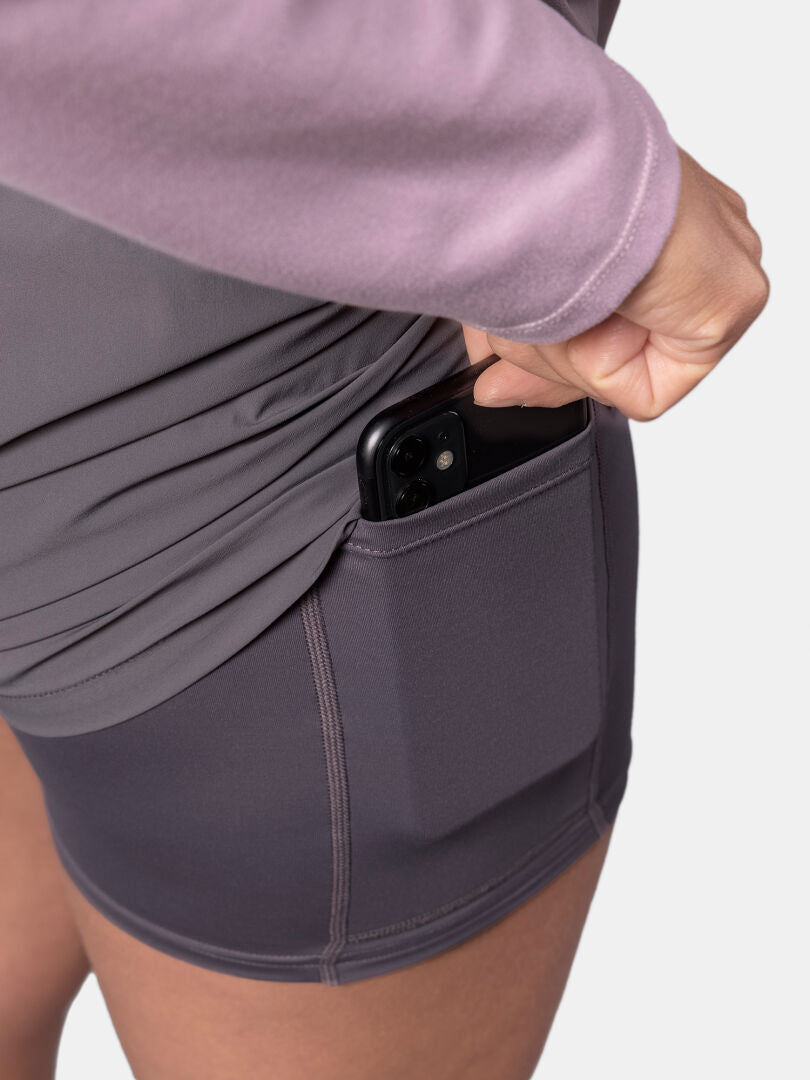 Kvinna stoppar en svart smartphone i sidofickan på Halti Uurto Shorts Dam, kombinerad med en lila topp.