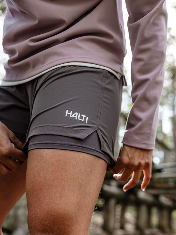 En person i Halti Uurto Shorts Dam och en långärmad tröja står utomhus nära en träkonstruktion.