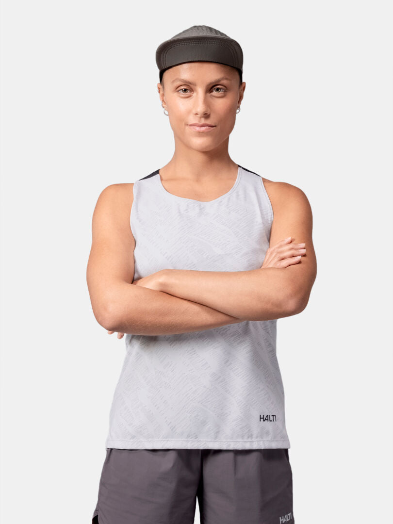 Person i grå Halti Oulanka Träningstopp Dam och shorts står med armarna i kors mot en enfärgad bakgrund.