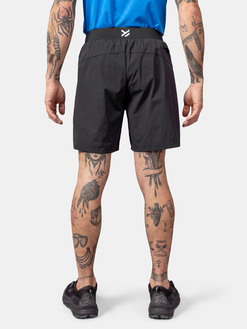 En person i blå skjorta och Halti Uurto Shorts Herr, med tatueringar på armar och ben, sedd bakifrån.