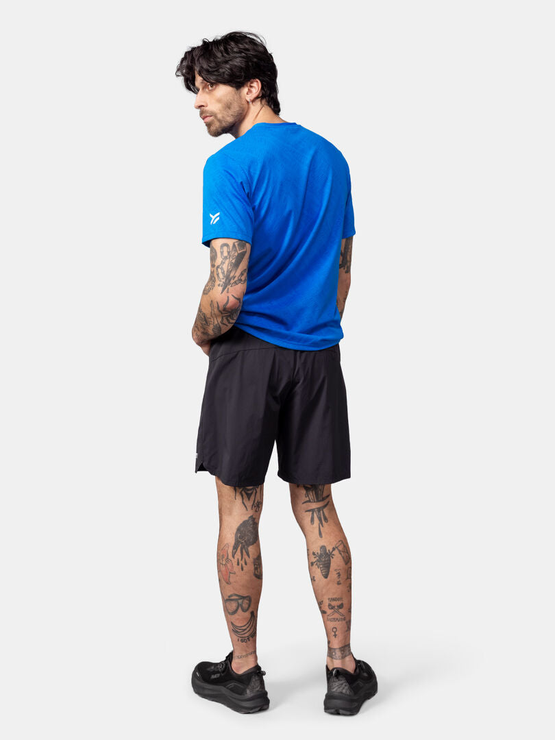 En man med tatueringar bär en Halti Oulanka T-skjorta Herr, svarta shorts och skor, och står med ryggen mot kameran.