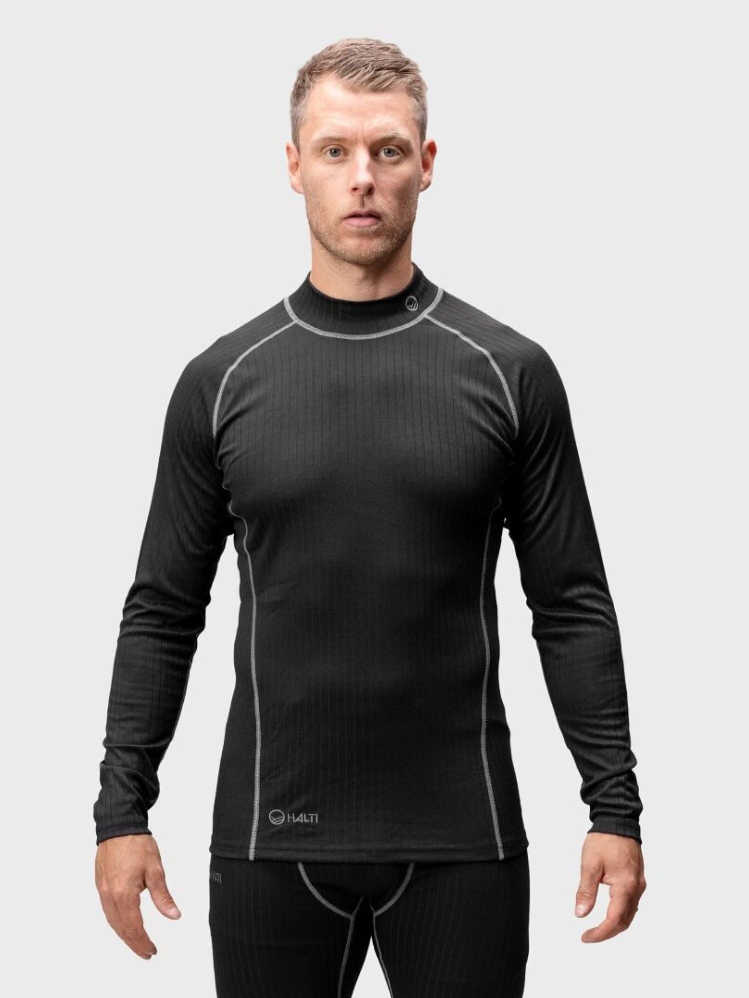 En man som bär Halti Dual Underställ Set Herr står mot en ljusgrå bakgrund.