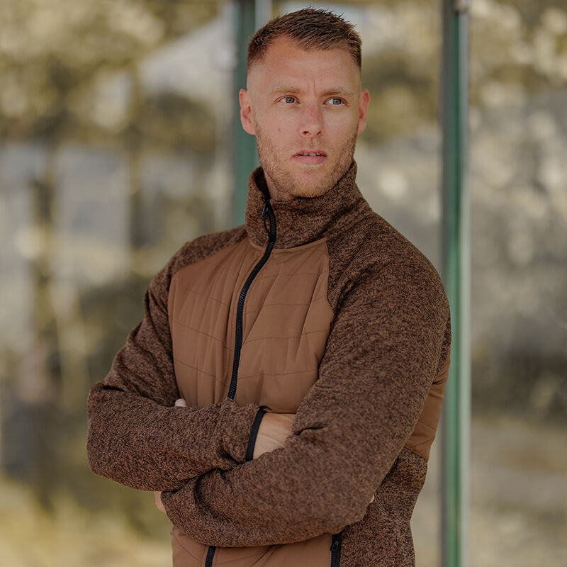 En man i en Halti Streams Hybrid Mellanlager Herr tillverkad av återvunnet material står med armarna i kors och tittar åt sidan.