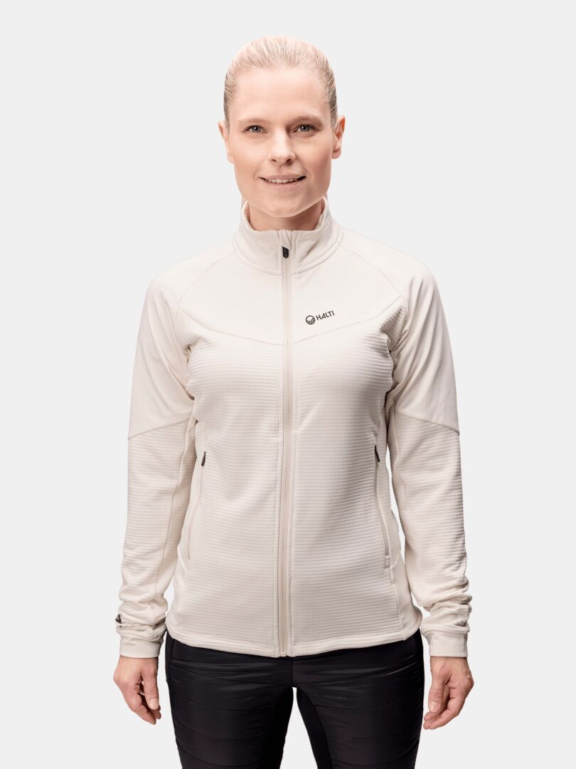 En ljushårig person bär Halti HeatGrid Mellanlager Dam, tillverkad av återvunnen polyester, mot en enfärgad bakgrund.