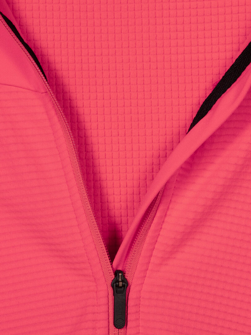 Närbild av en delvis uppknäppt rosa Halti HeatGrid Mellanlager Dam på texturerat tyg med rutmönstrad bakgrund.