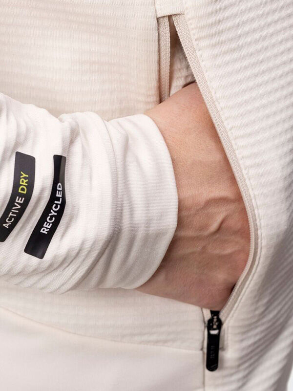 En hand i fickan på Haltis HeatGrid Mellanlager Dam, tillverkad av återvunnen polyester med Active Dry på ärmen.