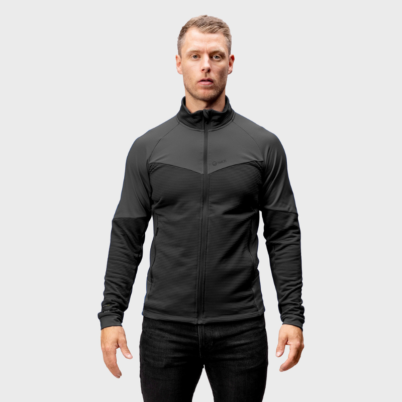 En man vetter framåt i en Halti HeatGrid Mellanlager Herr-jacka av återvunnen polyester, mot en ljusgrå bakgrund.