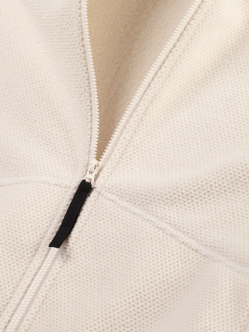Närbild på Halti Soolo Mellanlager Dam, en minimalistisk benvit jacka med strukturerat tyg och svart dragkedja.