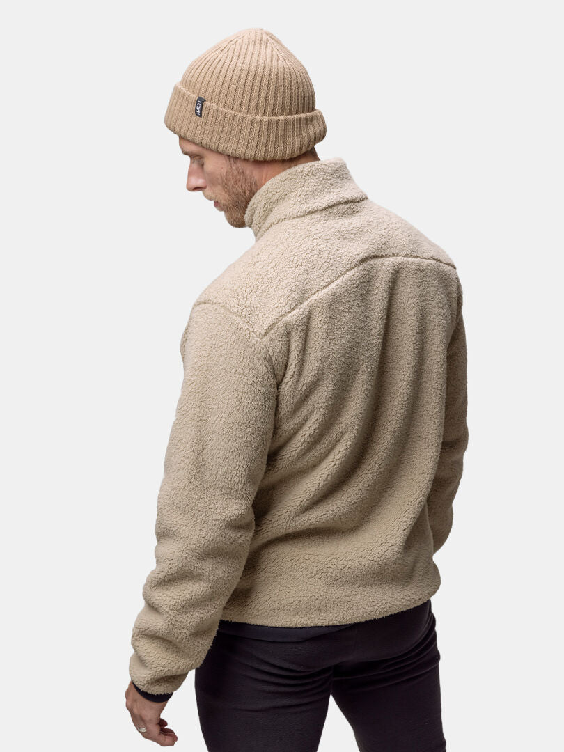 En man i Halti Lumista Polar Fleecejacka Herr och ribbad beige mössa står vänd bort mot en ljus bakgrund.