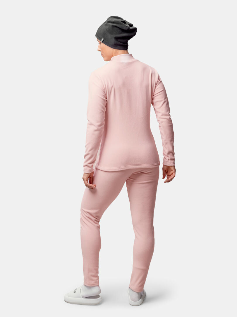 En person klädd i Halti Trone Fleece Tröja Dam och byxor, grå mössa och vita skor står vänd mot en enfärgad bakgrund.