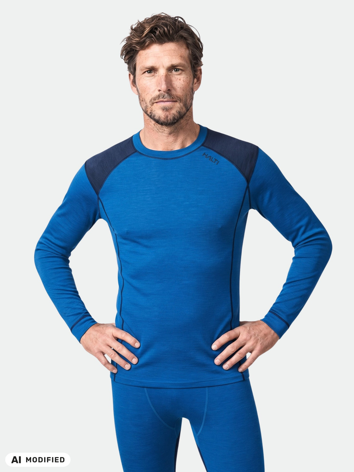 En man i Halti Hossa II Merino Underställ Set Herr – blå tröja och leggings – står med händerna på höfterna.