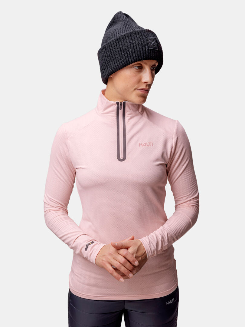 Person med rosa Halti Jaako Tröja Dam och mörk mössa, stående mot ljus bakgrund.
