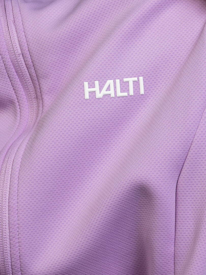 Närbild på Kivikko Mellanlager-damens strukturerade, ljuslila tyg med Halti-logotypen och en synlig dragkedjesöm på vänster sida.