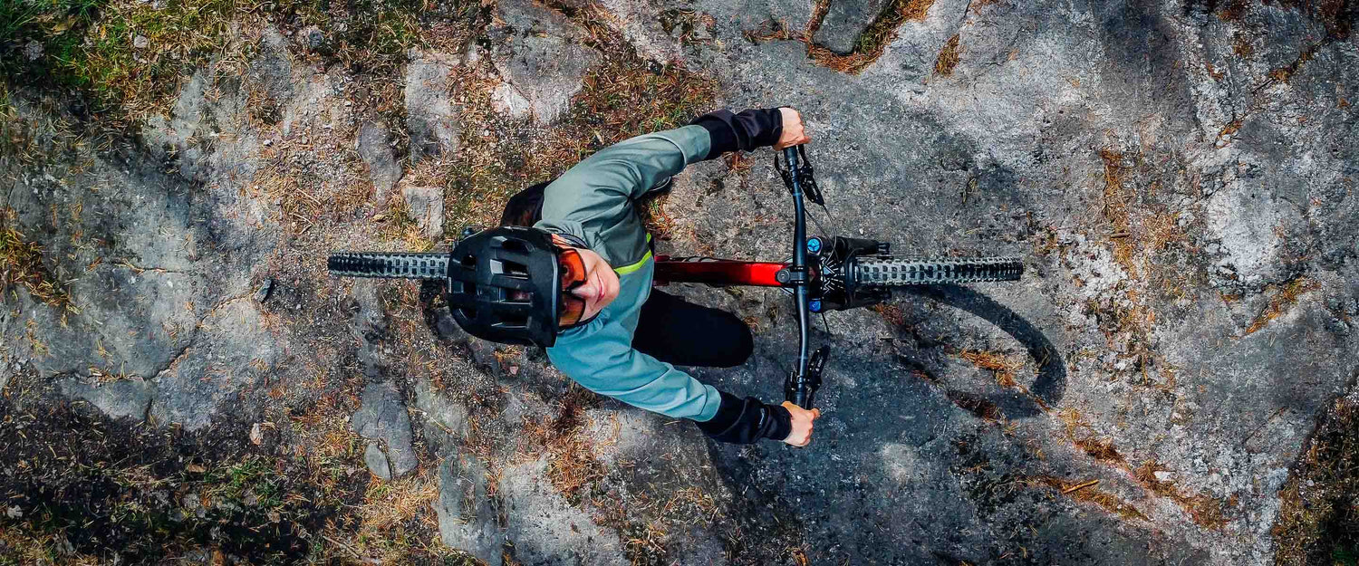 En person med hjälm cyklar på en mountainbike på en stenig yta, sett uppifrån.