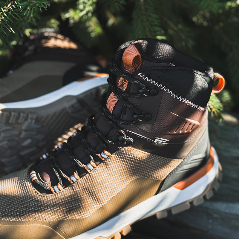 Närbild av Halti Kajava DrymaxX Outdoorskor Dam med orange accenter, snörad med tallgrenar och redo för äventyr.