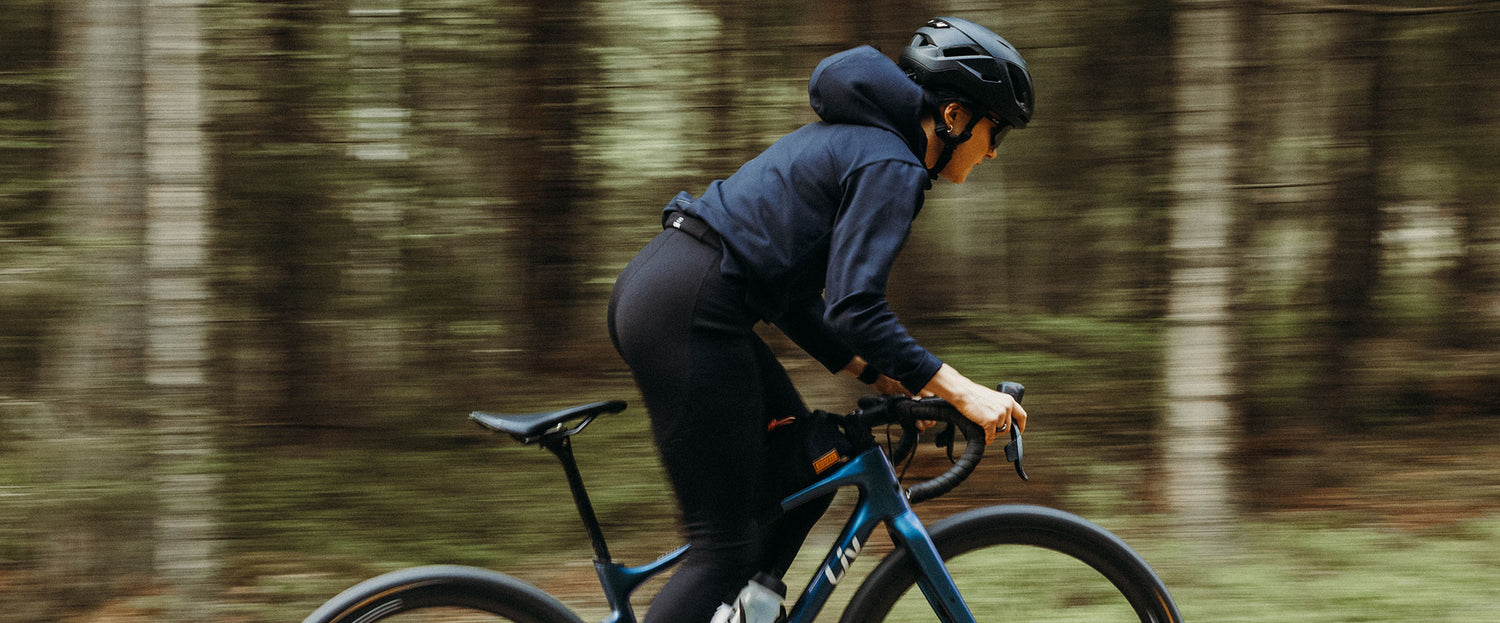 En person med hjälm cyklar på en blå cykel genom ett skogsområde.