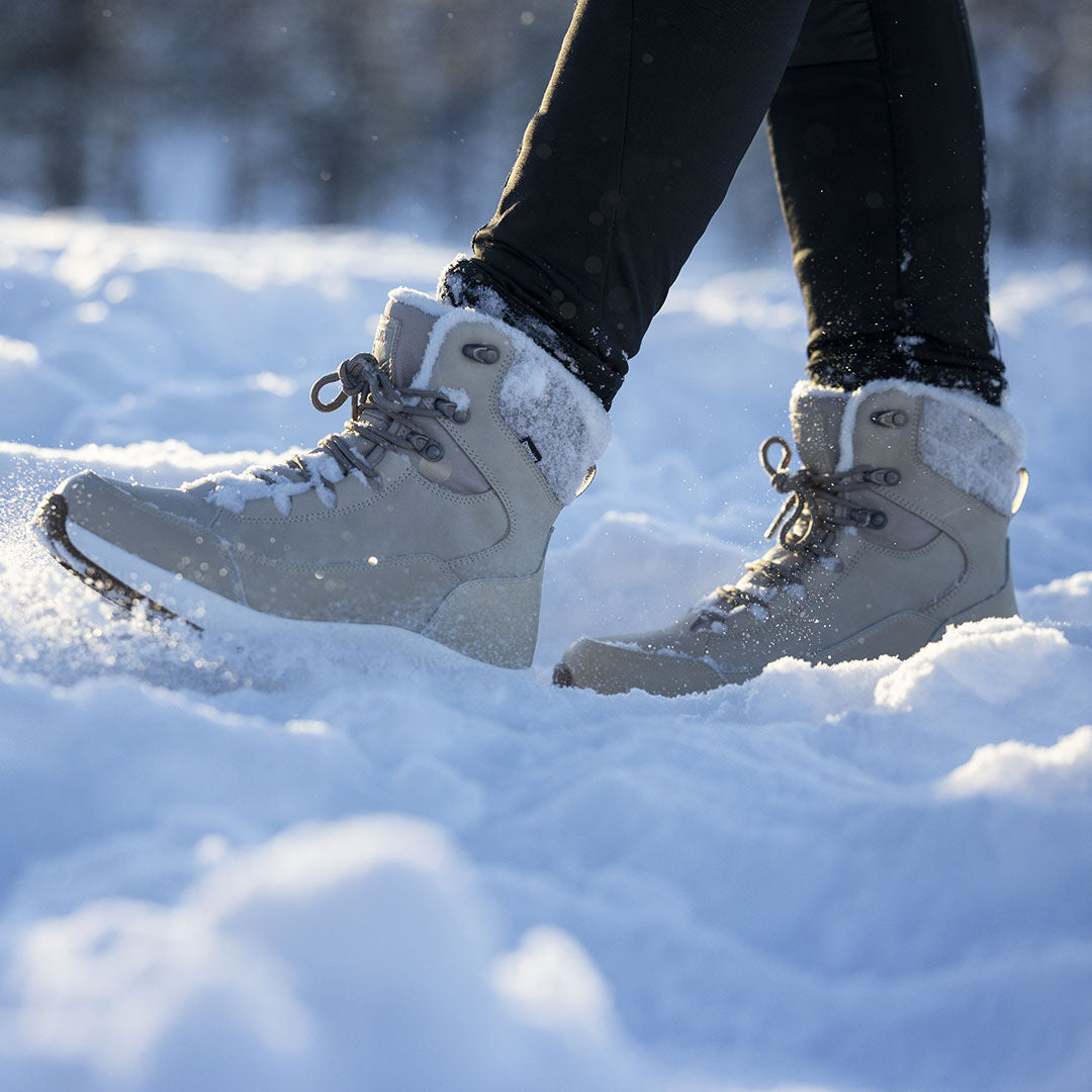 Person i svarta byxor bär Halti Dundee Mid DX vinterskor och går på solbelyst snö utomhus.