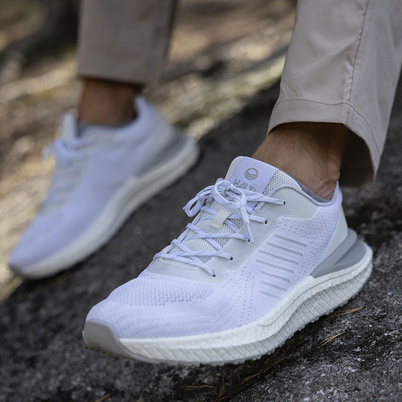 Person som bär Halti Gale Sneaker Herr i ljusgrå polyester och beige byxor står på en ojämn utomhusyta.