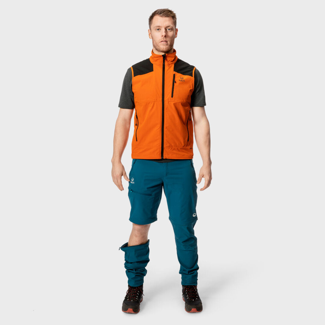 En man vetter framåt iförd Halti Pallas Herr X-stretch Väst, blå byxor och svarta vandringskängor mot en enfärgad bakgrund.