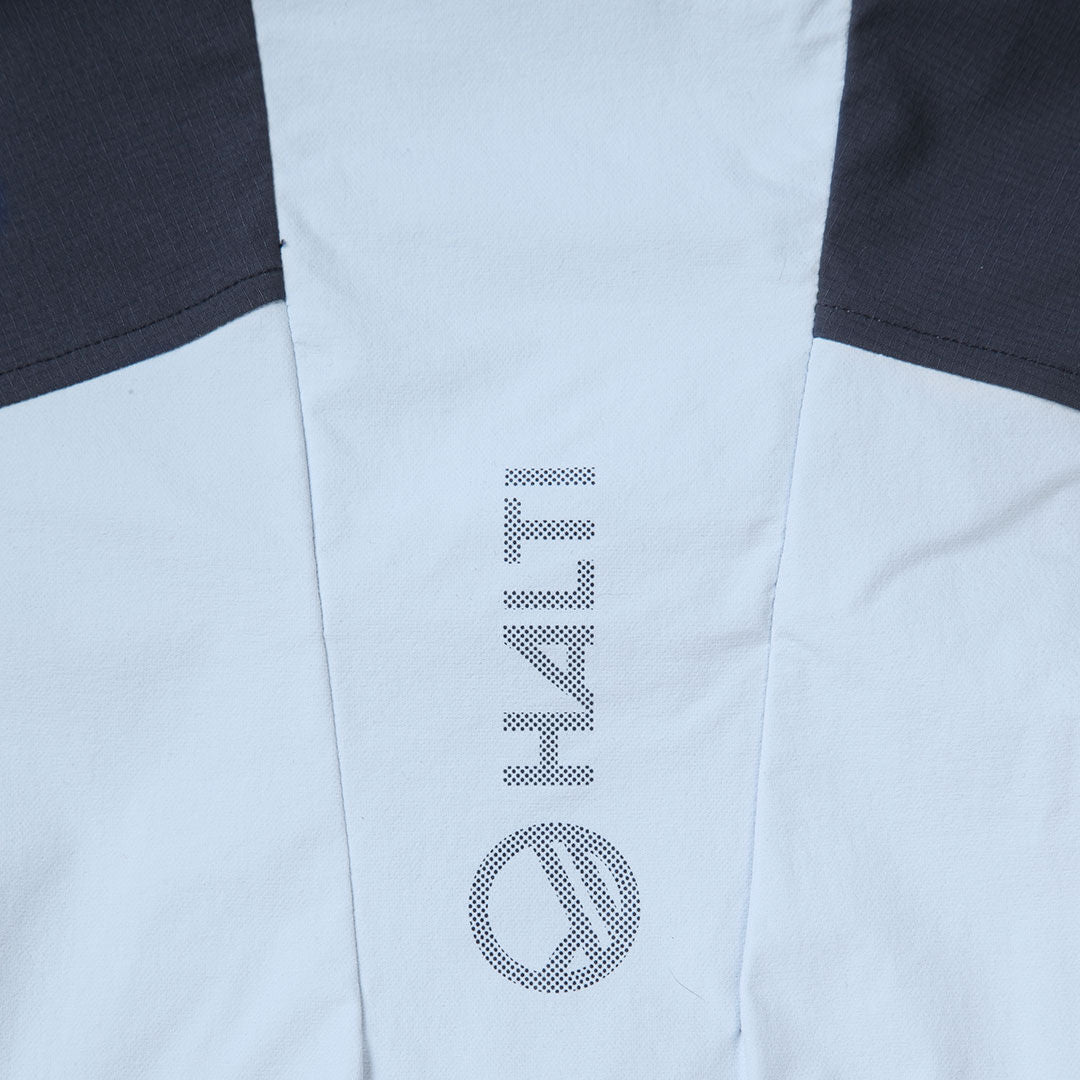 Närbild av det ljusgrå Pallas II X-stretch Jacka Dam-tyget med Haltis logotyp och namn i vitt och svart.