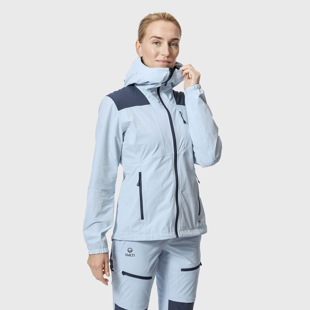 Person med Halti Pallas II X-stretch Jacka Dam i ljusblå/navy med matchande byxor, mot en enfärgad bakgrund.