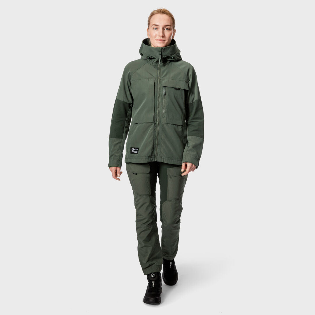 Person som bär Halti Hiker Dam Ventilated Jacka och byxor, gående framåt mot en ljusgrå bakgrund.