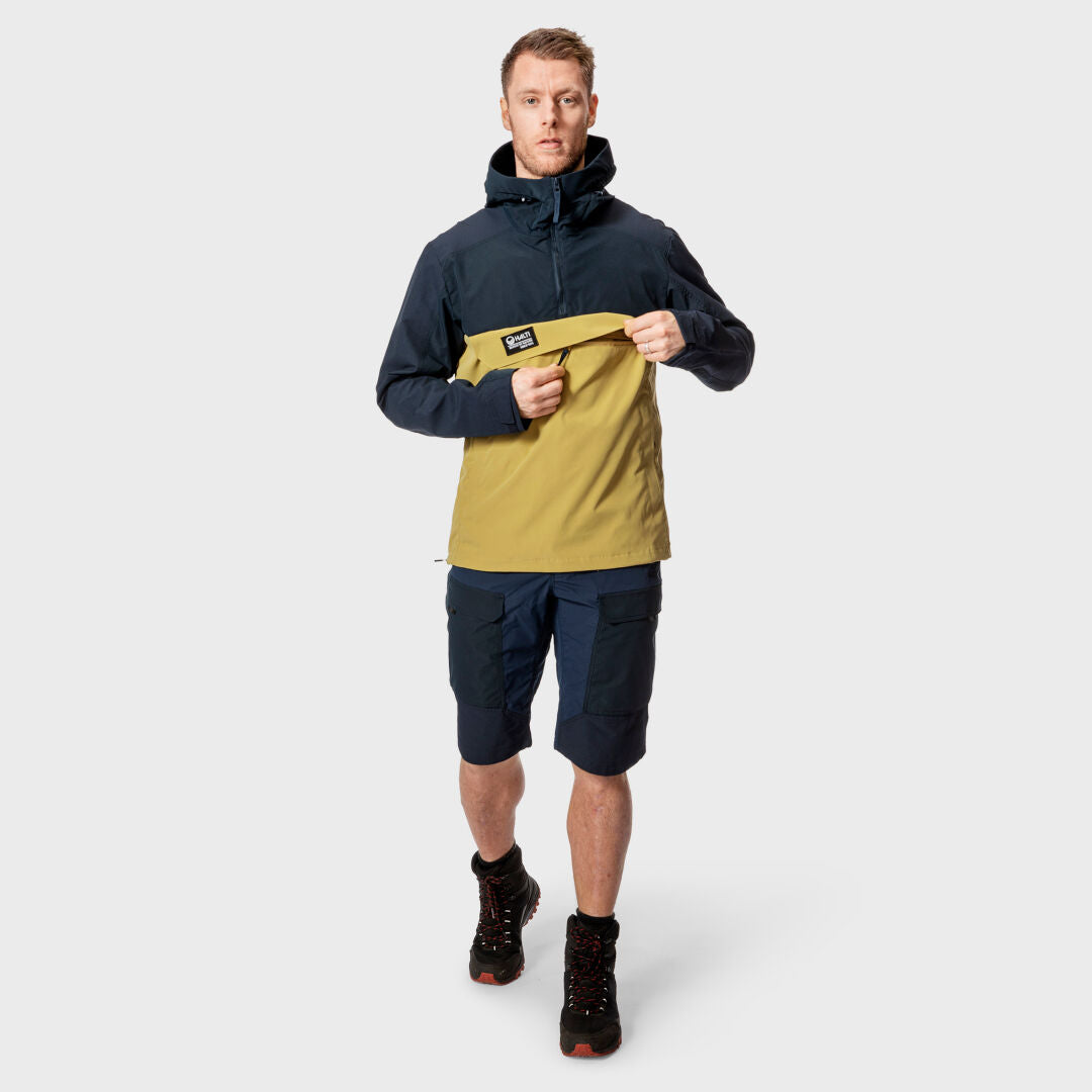 En man i en tvåfärgad jacka och Halti Hiker Herr Lite Shorts står vänd framåt mot en vit bakgrund.