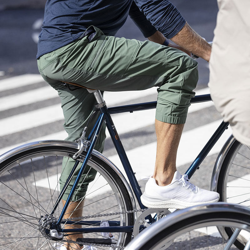 Iklädd gröna joggingbyxor och Halti's Gale Sneaker Herr cyklar en person över ett övergångsställe på en gata.
