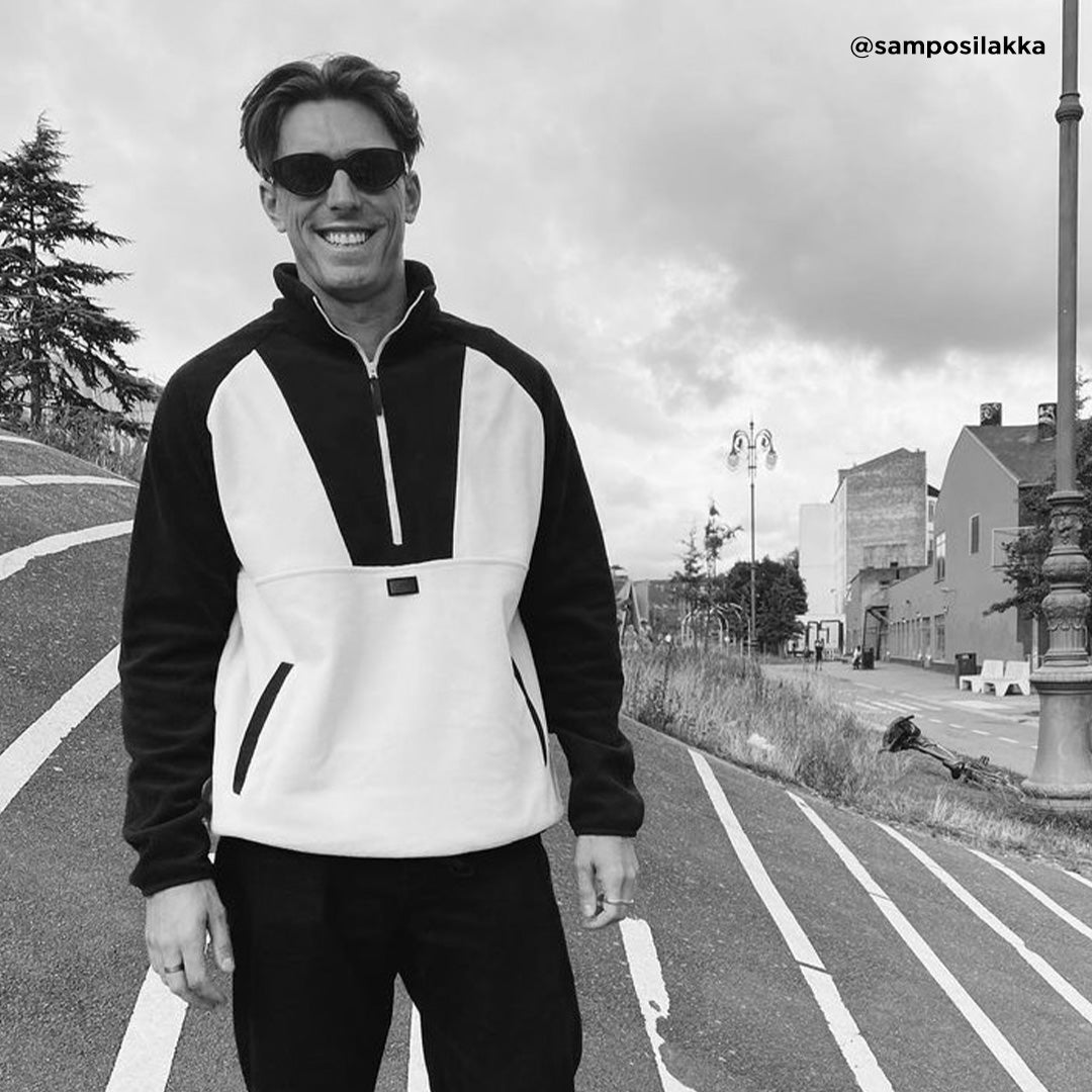 En man i solglasögon och en Halti Skugge Unisex Fleece Anorak ler utomhus och visar upp sin athleisure-stil.