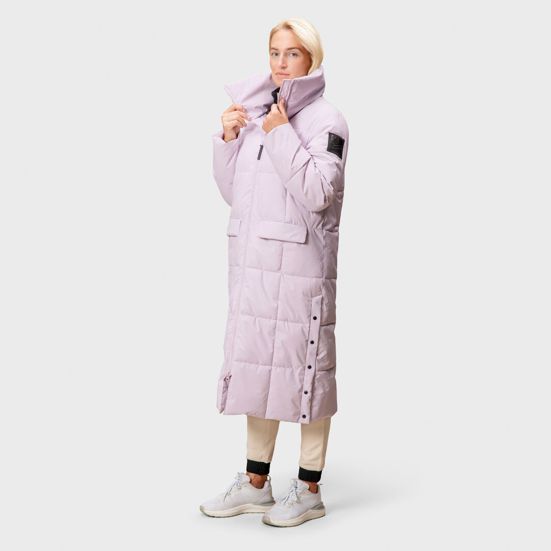 En person bär en lång, ljuslila Halti Penger Vinterjacka Dam pufferjacka med beige byxor och vita sneakers.