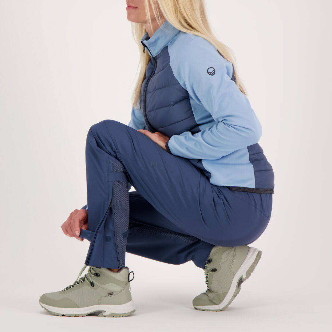 En person med långt blont hår sitter på huk i blå friluftskläder och Halti Liike Dam 3L DrymaxX Sport Byxor.