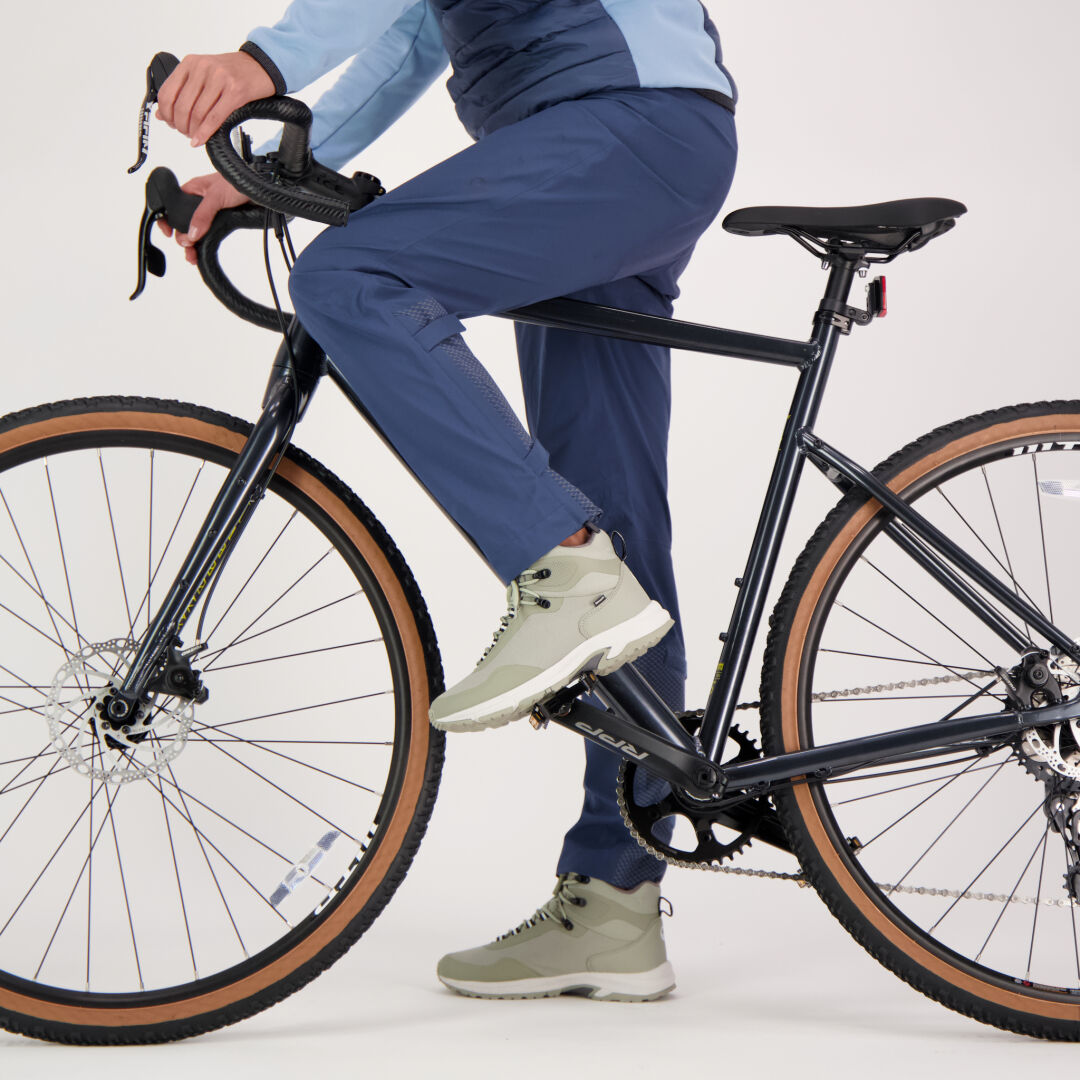 En person i Halti Liike Dam 3L DrymaxX Sport Byxor och ljusgrå sneakers sitter på en svart cykel mot vit bakgrund.