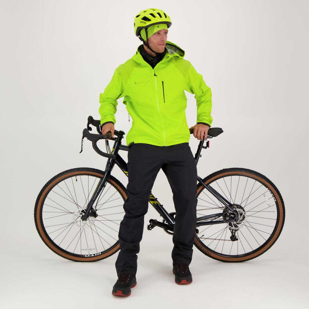 En person i Halti Liike Herr 3L DrymaxX Sport Byxor står vid en svart cykel mot vit bakgrund.