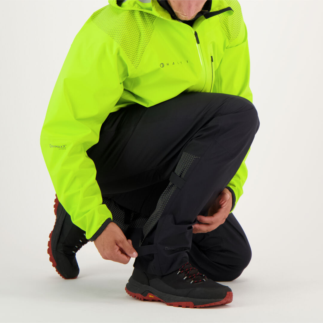 En person i gul jacka sätter fast Halti Liike Herr 3L DrymaxX Sport Byxor över svarta byxor.