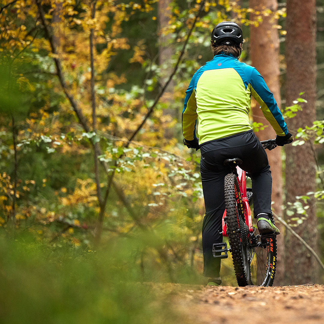 Iklädd en Halti Suunta Herr Hybrid Jacka och hjälm cyklar en person mountainbike på en höstskogsstig.