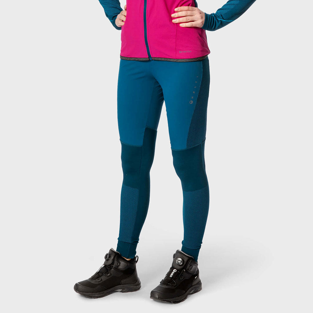 En person i rosa jacka, Halti Tracks Seamless Tights Dam och svarta stövlar står mot en vanlig ljus bakgrund.