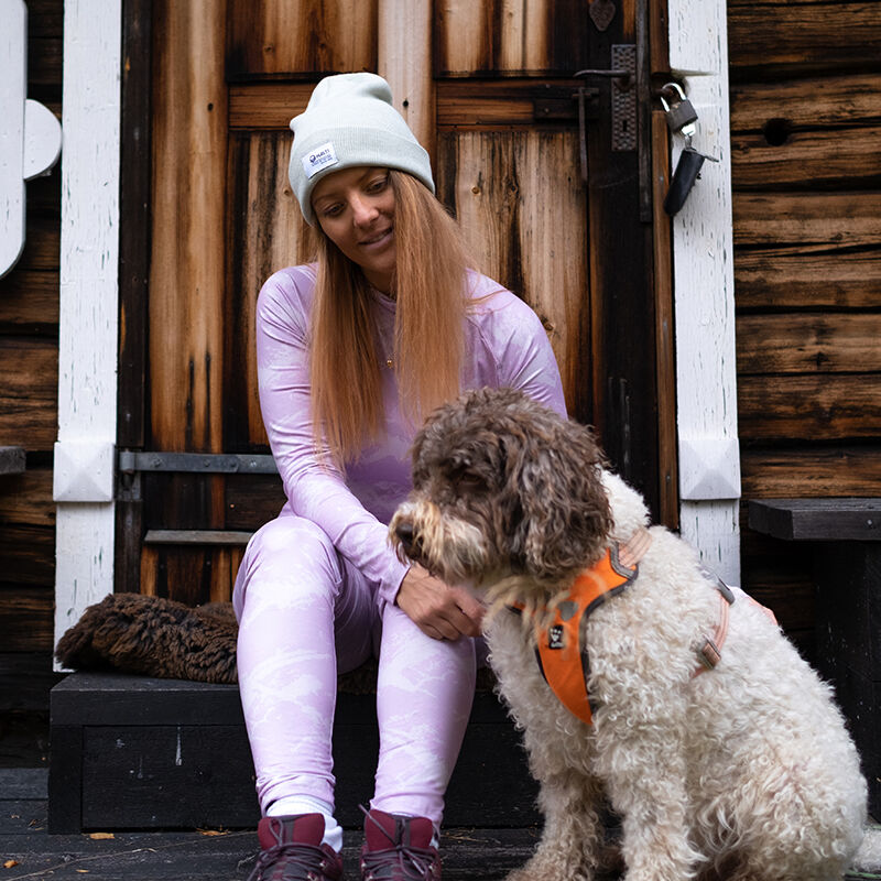 En kvinna i en Halti Windfire Underställsset-damm sitter på trätrappor bredvid en hund i orange sele.