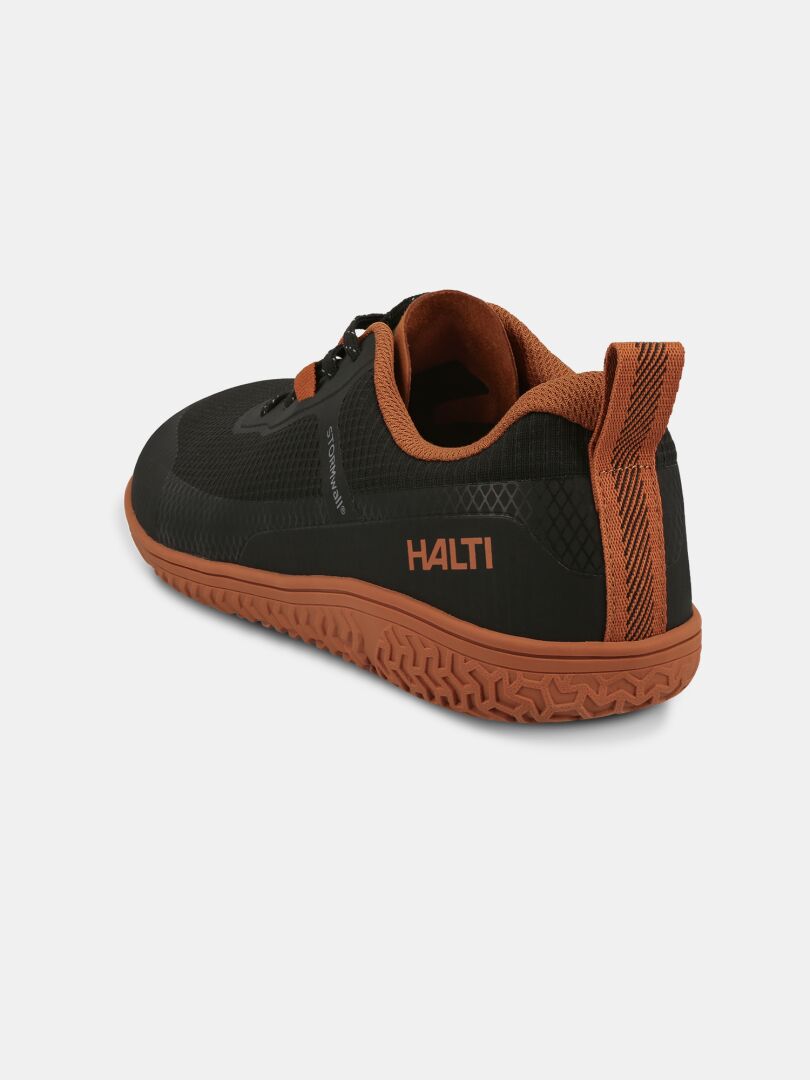 Halti Tuntuma Barfotaskor: svart/brun unisexsko med strukturerad sula, orange foder, noll-drop-läst, logo på sidan.