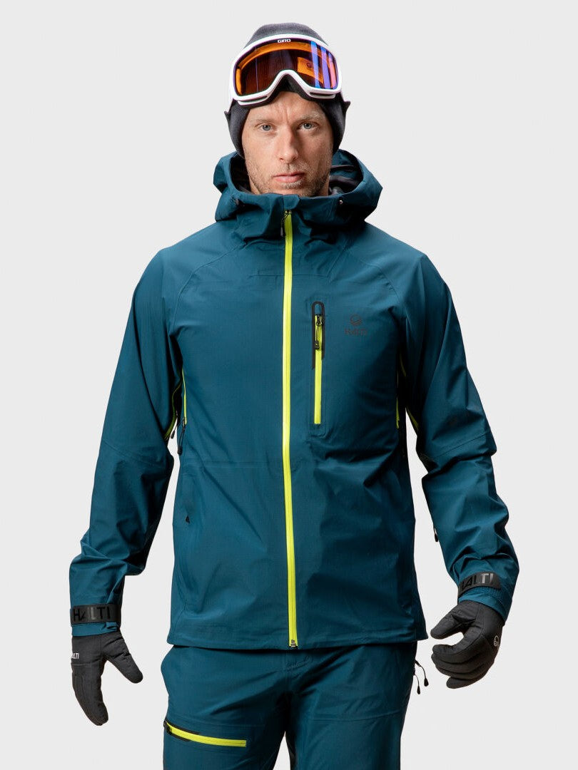 En person i blå Halti Alpine Unisex 3L DrymaxX skaljacka, matchande byxor, handskar och skidglasögon.