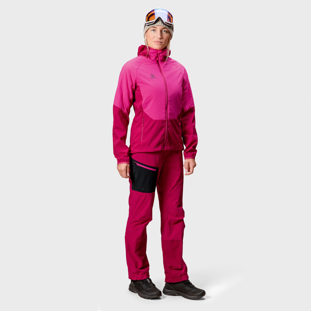 Någon bär Halti Crust Dam Mellanlagerjacka i rosa med byxor, svarta skor och skidglasögon, vänd framåt.