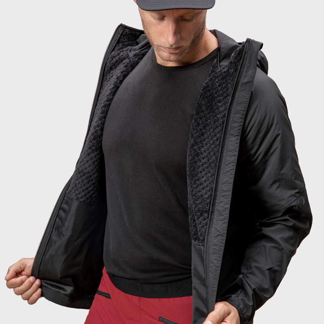 En man i Halti Crust Herr Mellanlagerjacka öppnar den och visar dess texturerade foder och X-stretchmaterial inuti.