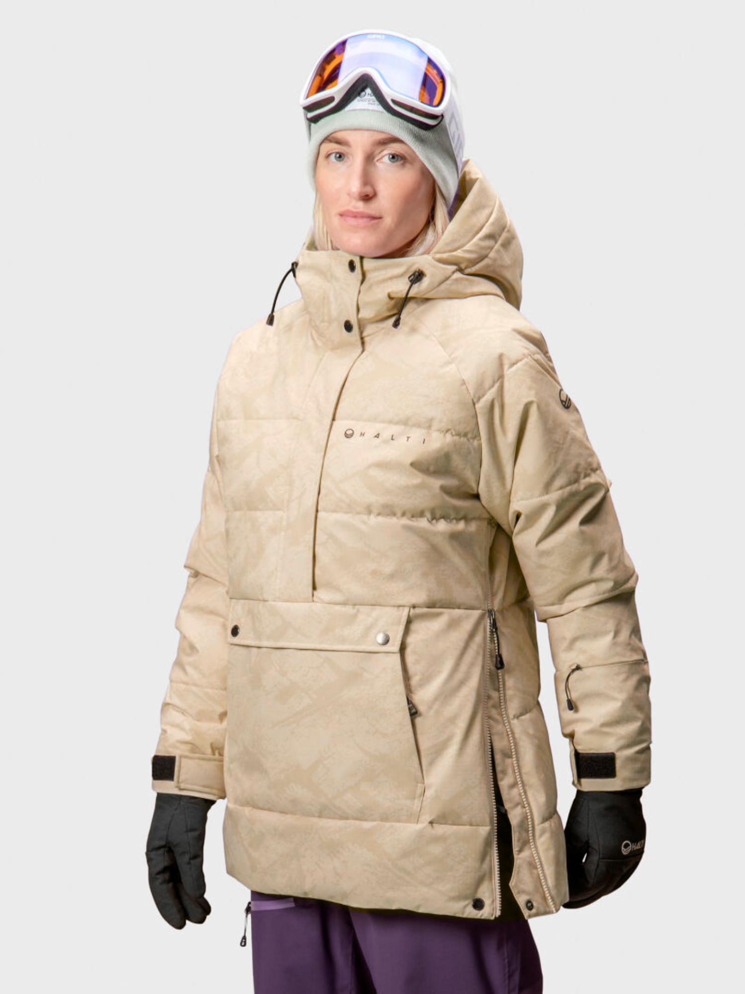 En person bär en beige Halti Chowper Skidanorak Dam med DrymaxX, plus handskar, mössa och skidglasögon.